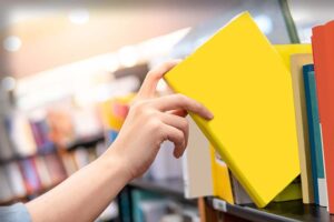 書店の本棚から黄色い表紙の本を手に取る女性の手